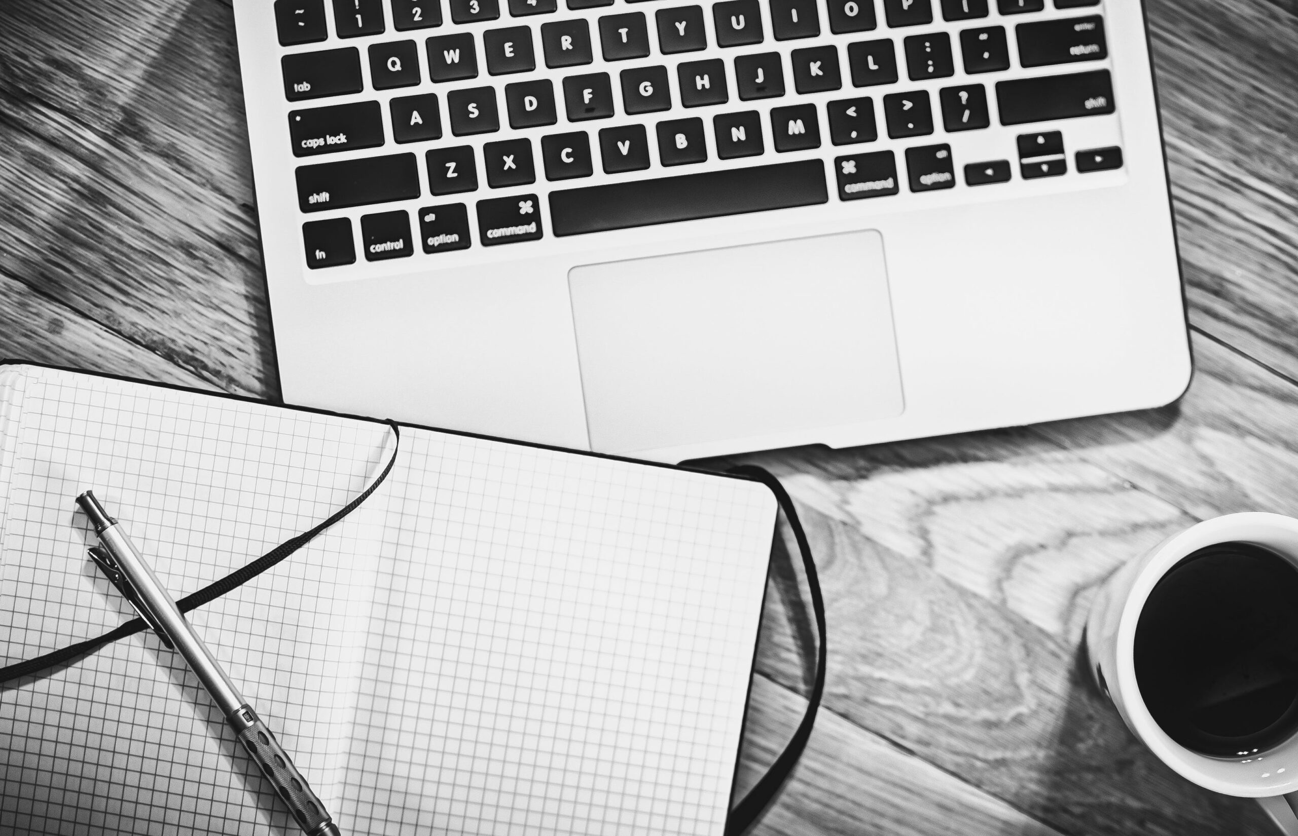 Overhead view of an open graph notebook, a laptop keyboard and a cup of coffee.